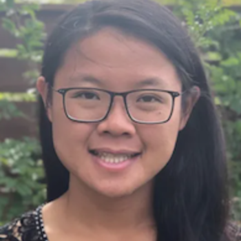 A headshot of Jean - she is smiling and wearing glasses and a black shirt with white polka dots. She has long black hair