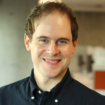 A photo of Stathis. He is smiling and wearing a dark blue button down shirt. He has short brown hair.