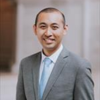 A headshot of Leo -- he is smiling and wearing a grey suit jacket and blue tie. He has very short/buzzed hair.