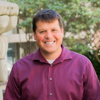 A photo of Patrick - he is wearing a burgundy button up shirt. He is smiling and has short cropped brown hair.