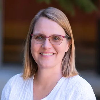 A headshot of Starley -- Starley is smiling and wearing glasses and a white shirt. She has shoulder length blonde hair. 