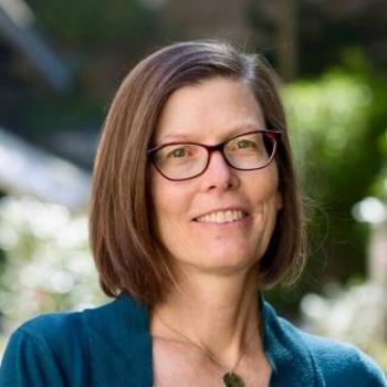 Sara smiling at the camera - she is wearing glasses and a teal shirt. She has chin length, straight brown hair.