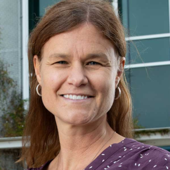 Christine smiling at the camera. Her reddish brown hair is partially tied back, and she is wearing a purple top.
