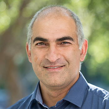 Ali smiling at the camera. He has short cropped salt and pepper hair and is wearing a blue collared shirt. 